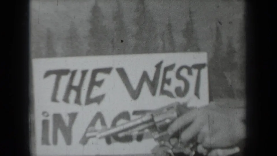 1937 Klamath, California 8mm frame showing a handmade The West in Action sign with a hand and toy revolver partly visible.
