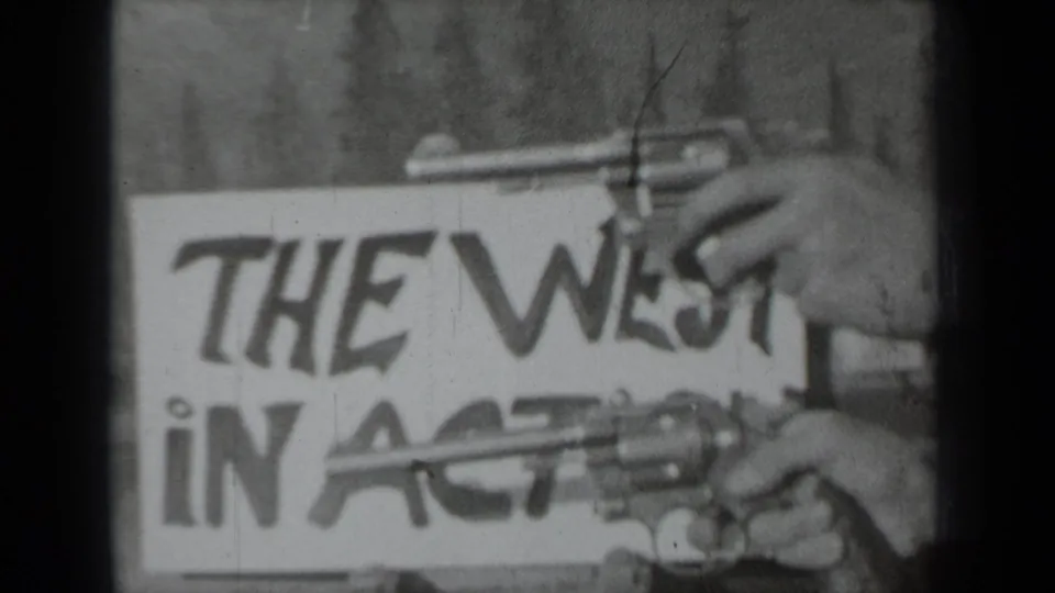 1937 Klamath, California home-movie frame with hands holding toy revolvers in front of a The West in Action placard.