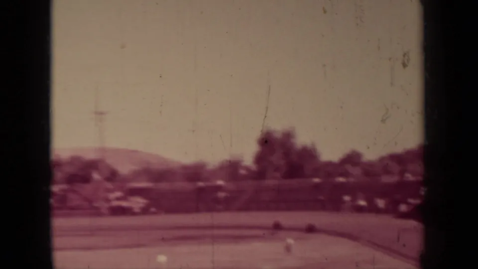1937 Klamath, California frame showing the edge of a baseball field with trees, low hills, and scattered activity in soft faded color.