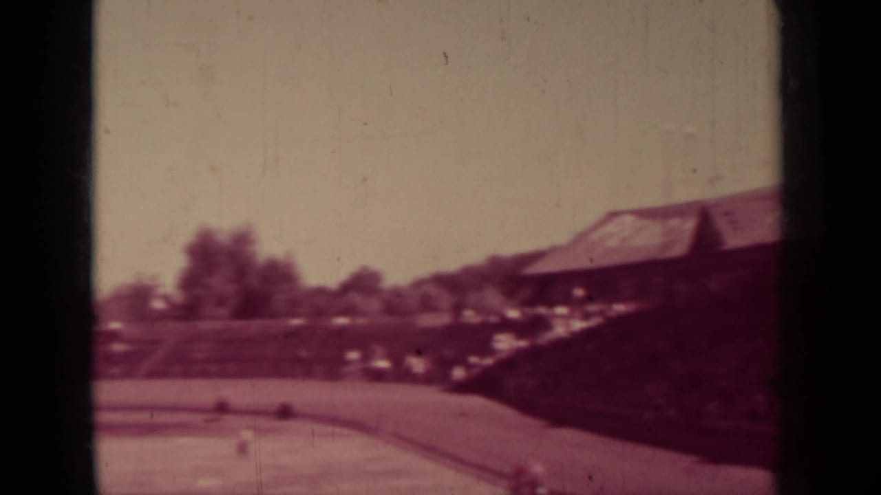 Ballfield edge and wooden grandstand seen through dark film gate bars.
