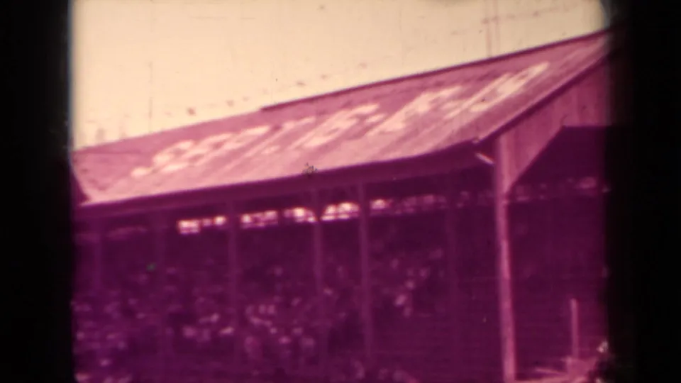 The home movie frames a packed section of the Klamath baseball stands, with spectators seated beneath a lettered roof.
