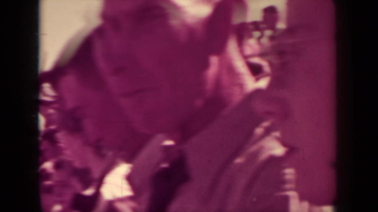 Soft 8mm close view of adults standing in a crowded Klamath public gathering, with faces partly obscured by exposure and motion.