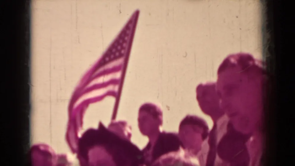 1937 Klamath home-movie frame with an American flag raised above spectators at a crowded outdoor public event.
