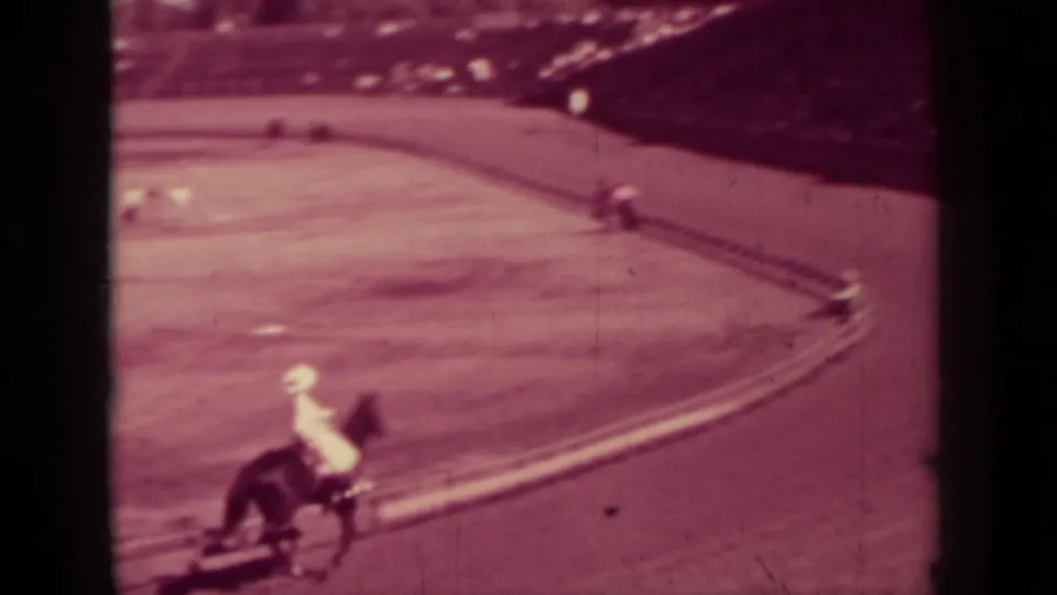 1937 Klamath, California home-movie frame showing a rider on horseback moving around a dirt track curve near the grandstand.