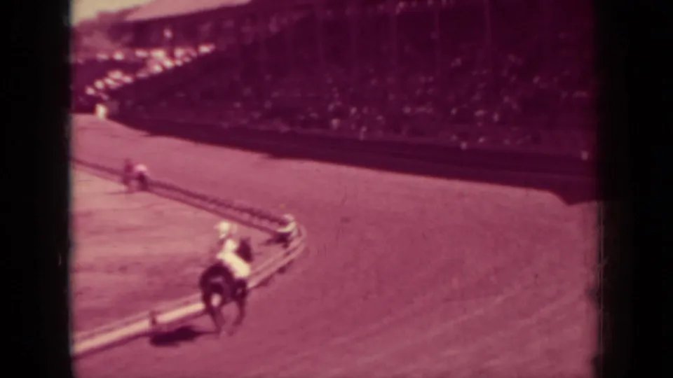 A mounted rider moves along the curve of a dirt racetrack in Klamath, California, with crowded wooden stands in the background.