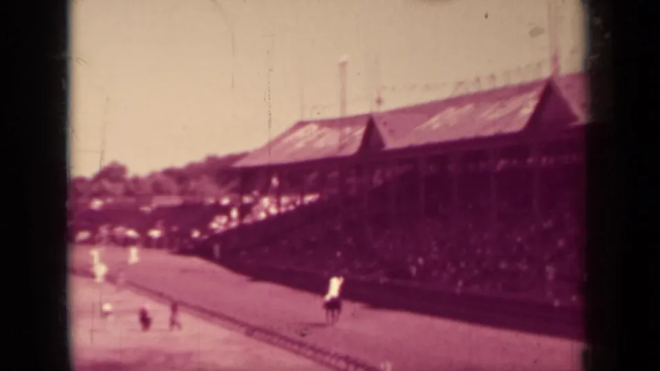 Wide 1937 home-movie view of a wooden grandstand beside a dirt horse track in Klamath, California, with riders below.