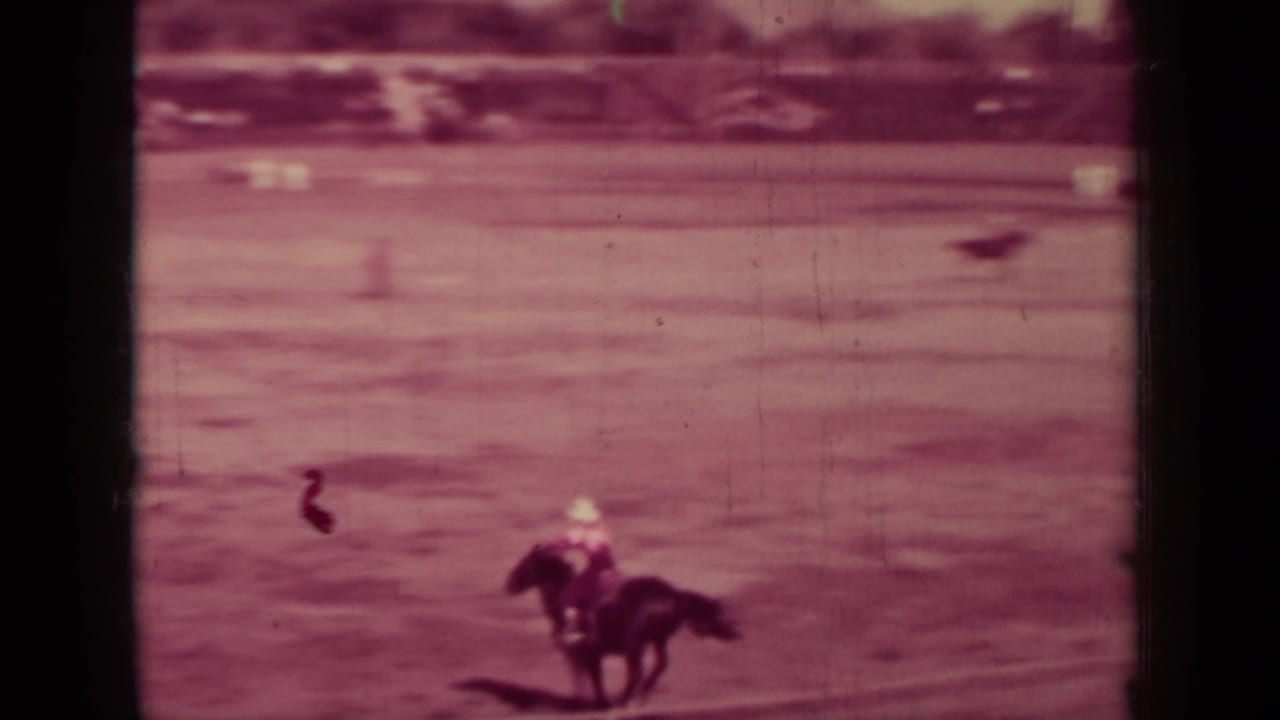 Mounted rider crossing a dusty arena with dark film borders and soft focus.