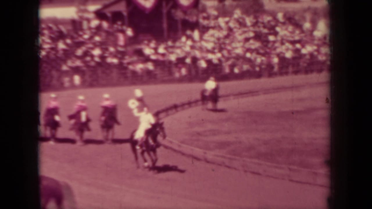 Several riders move around a curved dirt arena in front of crowded bleachers in Klamath, California, 1937.