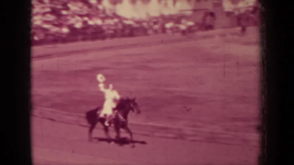 A light-clothed rider on a dark horse crosses the open arena in faded 8mm footage from 1937 Klamath, California.