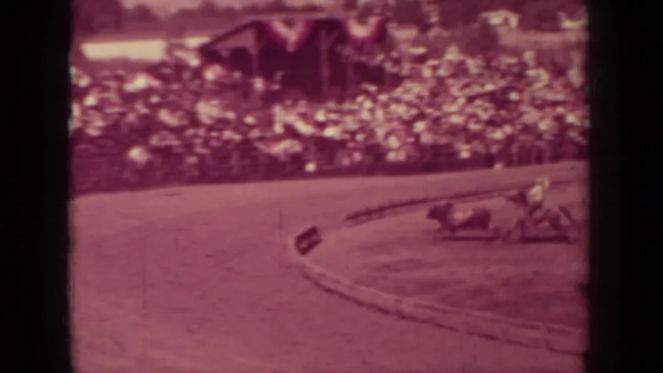 1937 Klamath, California home-movie frame showing horses and riders entering a curve before a large spectator crowd.
