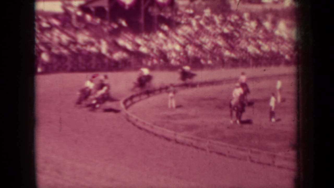 Klamath, California race scene with riders spaced around a dirt oval and a large crowd watching from the stands.