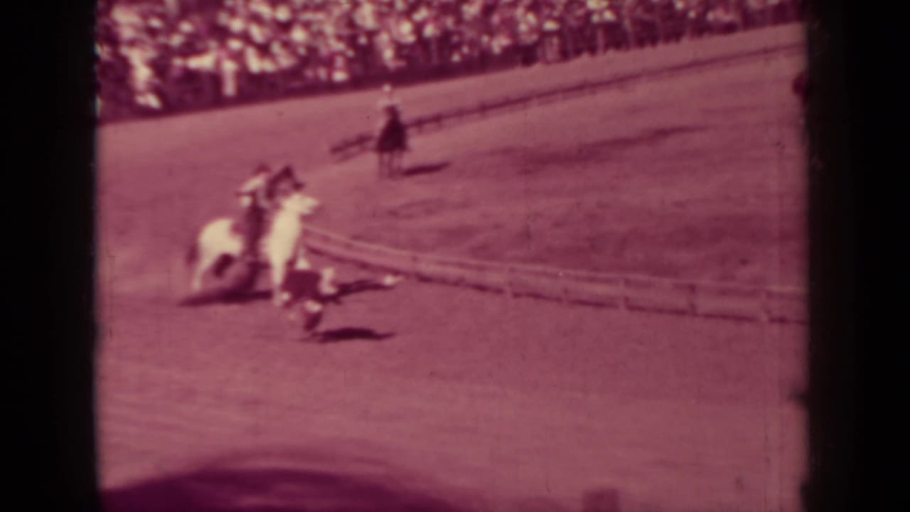Mounted rodeo riders converge near a calf on the arena ground, with a crowded rail behind them in 1937 Klamath footage.