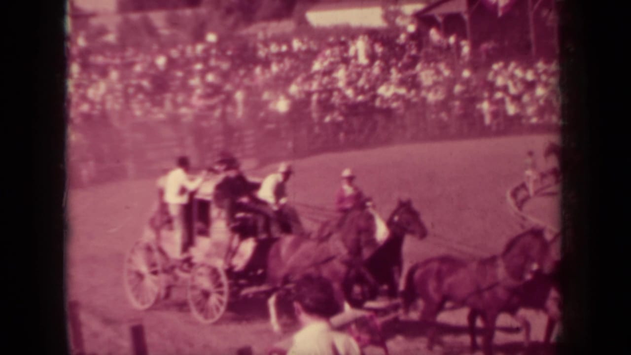 Horse-drawn carriages appear mid-race on a dirt oval at the Klamath, California fair, with spectators filling the stands.