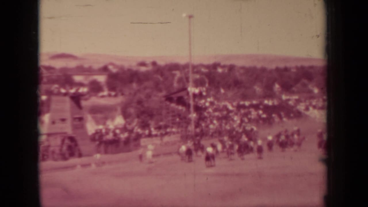 A wider home-movie view shows the fairground setting, with crowds near the track and trees beyond the grounds.