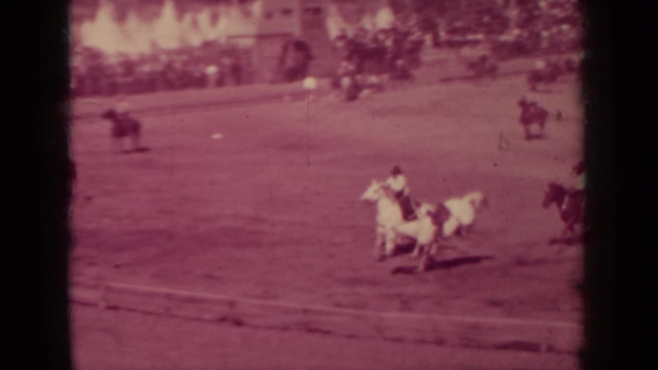 Riders on horses racing across a dirt track with dark film edges.
