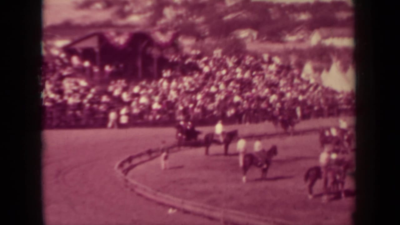 Horse riders round a dirt-track turn before a large crowd in the 1937 Klamath, California home-movie footage.