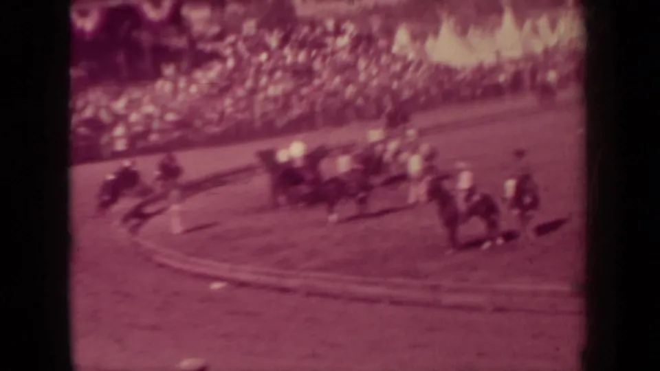 1937 Klamath, California home-movie frame showing horses and riders rounding a dirt fairground track with spectators in the stands.