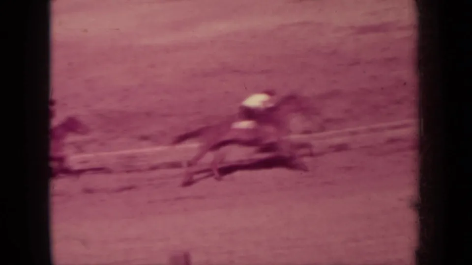 A horse and rider rush past the camera position in a motion-blurred 8mm frame, emphasizing the speed of the fairground race.