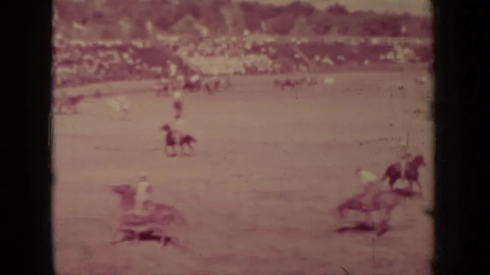 Wide 8mm view of a 1937 Klamath rodeo with mounted cowboys, bucking horses, and spectators lining the background.