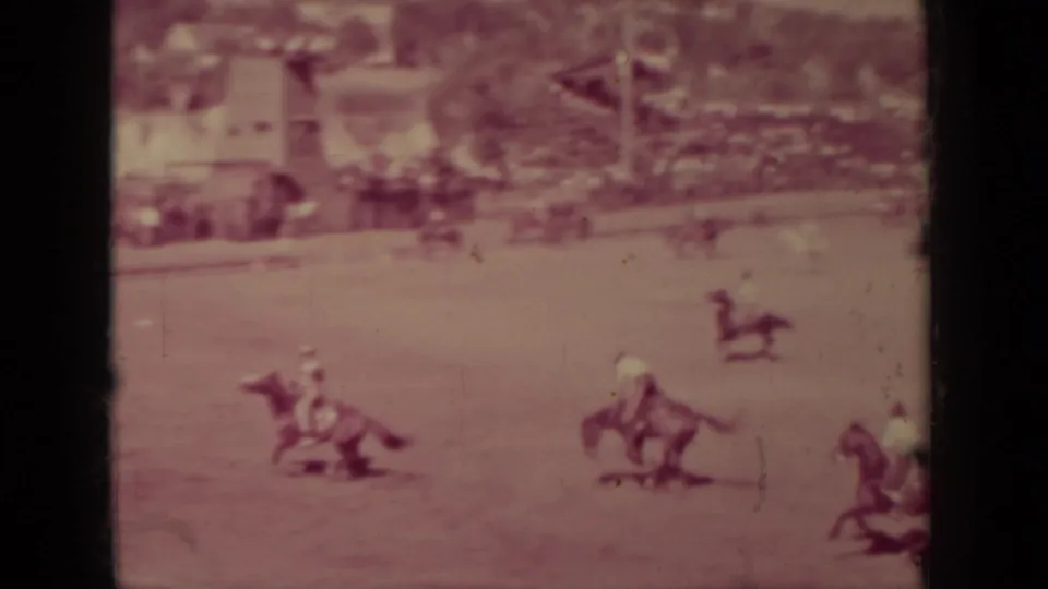 Pink-tinted 8mm frame from the Klamath, California rodeo showing several riders and horses across the arena.