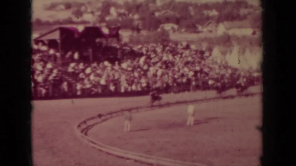 1937 Klamath, California frame with spectators packed near a covered stand as riders pass on the track curve.