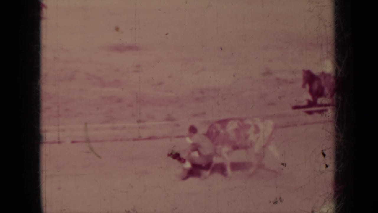 1937 Klamath, California home-movie frame showing a cowboy grappling with a spotted bull or steer as a rider watches in the arena.