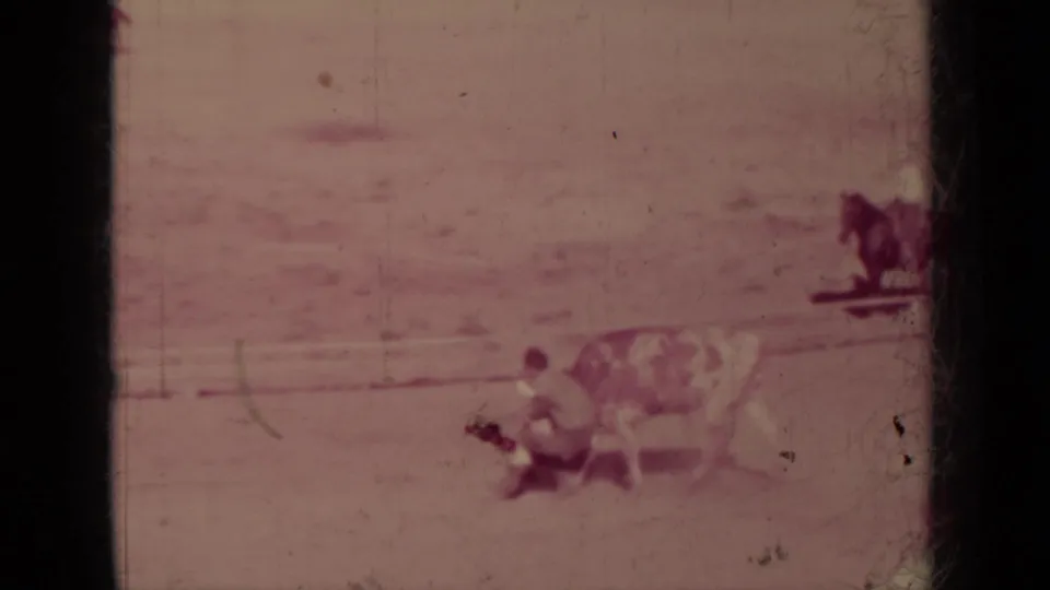 1937 Klamath, California home-movie frame showing a cowboy grappling with a spotted bull or steer as a rider watches in the arena.