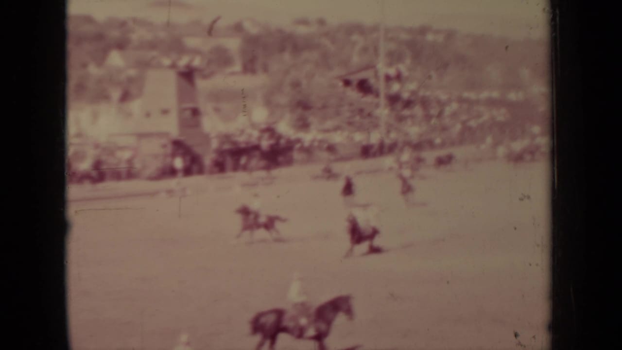 Faded 1937 Klamath 8mm frame showing a horse in the foreground area, distant riders, livestock, and small buildings beyond.