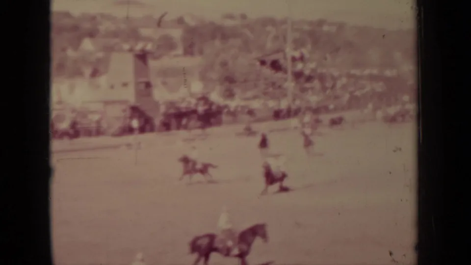 Faded 1937 Klamath 8mm frame showing a horse in the foreground area, distant riders, livestock, and small buildings beyond.
