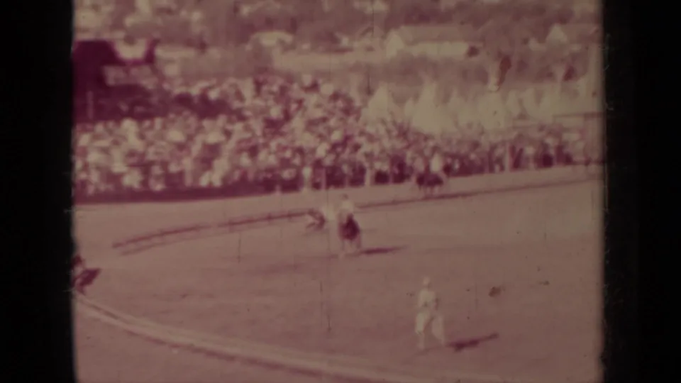 A wide 1937 Klamath rodeo frame with a rider and livestock near the arena rail while spectators fill the background stands.