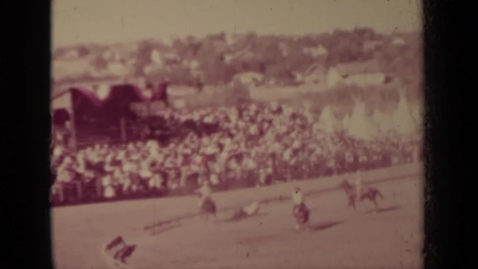 Wide home-movie view of the Klamath rodeo crowd and arena, with riders and livestock visible near the fence line.