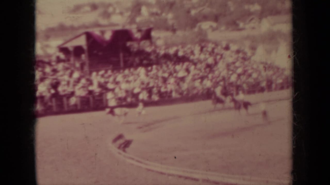 Late frame from the 1937 Klamath rodeo showing arena action in front of crowded bleachers and a small roofed structure.