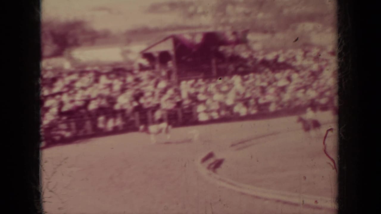 Horse riders move across a dirt arena in front of crowded bleachers.