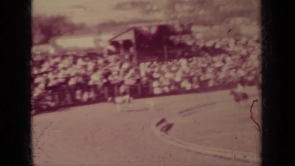 1937 Klamath, California 8mm frame showing riders on a dirt track with spectators seated along the arena edge.