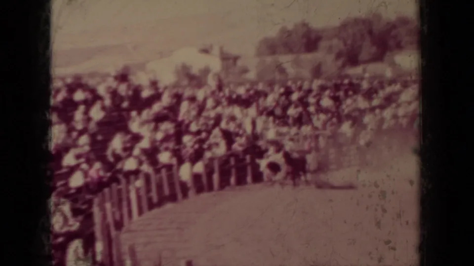 1937 Klamath, California 8mm frame showing a dusty rodeo arena bordered by fencing and crowded spectator bleachers.