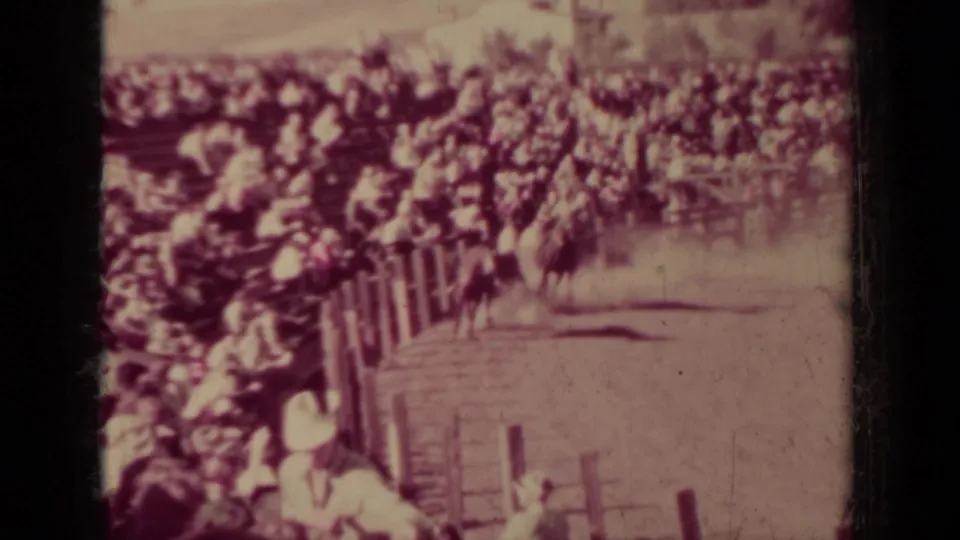 Wide 8mm view of a Klamath rodeo arena, with onlookers packed behind fencing and a horse or livestock shape near the rail.