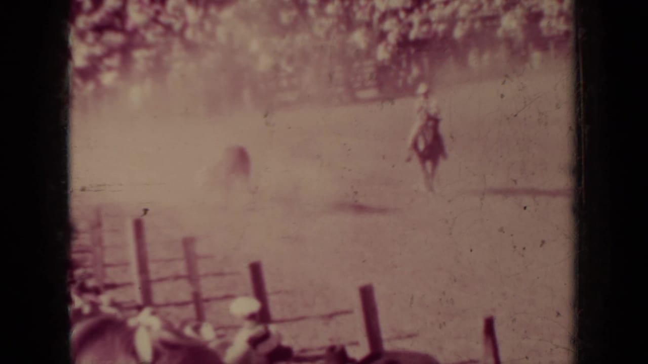 Distant rider on horseback in a rodeo arena with spectators and fence rails.