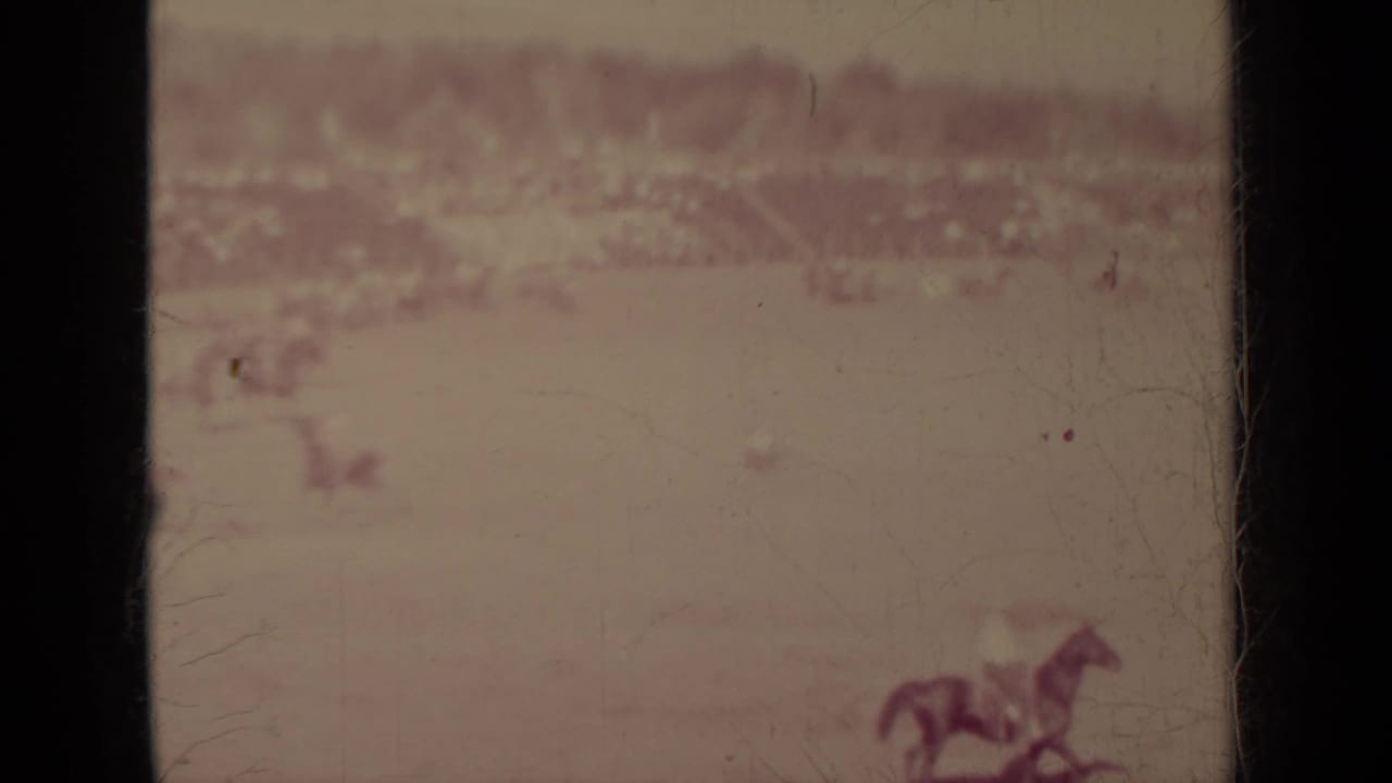 A horse and rider appear near the right edge of a wide dusty field.