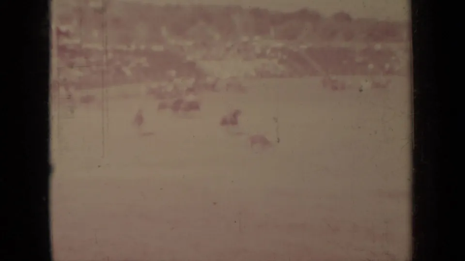 Several faint riders and horses occupy the open field in this aged 8mm frame from the Klamath equestrian scene.