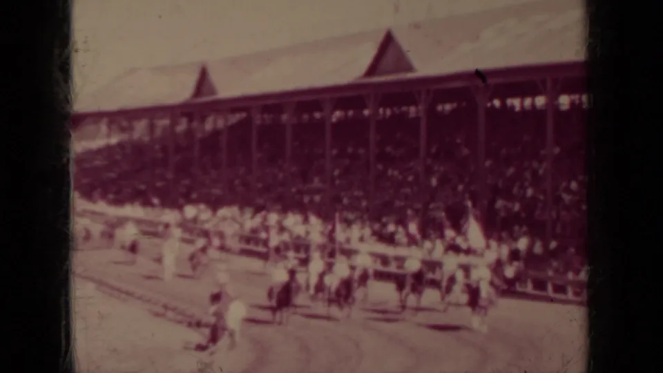 1937 Klamath race event frame with mounted horses and handlers near the rail before a packed covered grandstand.