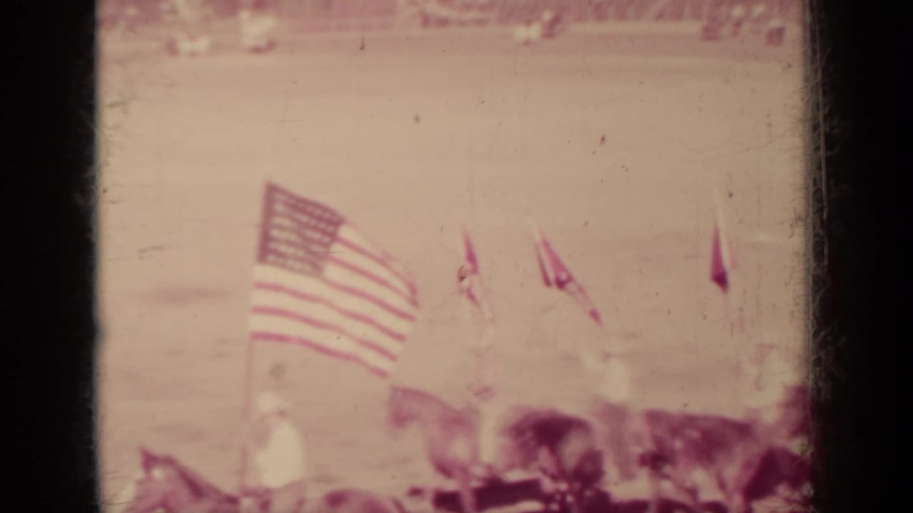 Riders and American flags in a dirt arena before a blurred grandstand.