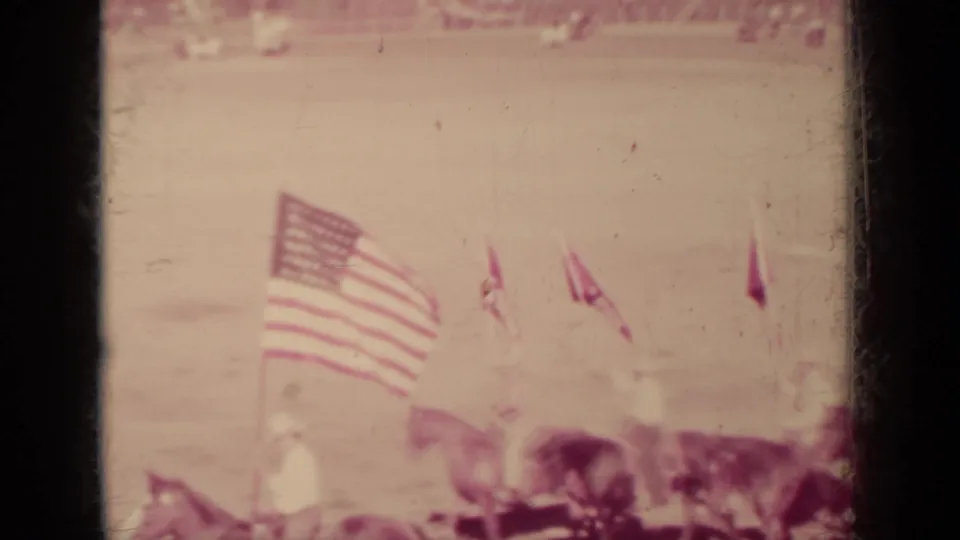 1937 Klamath, California home-movie frame showing riders and large American flags during a horse ceremony in a dirt arena.