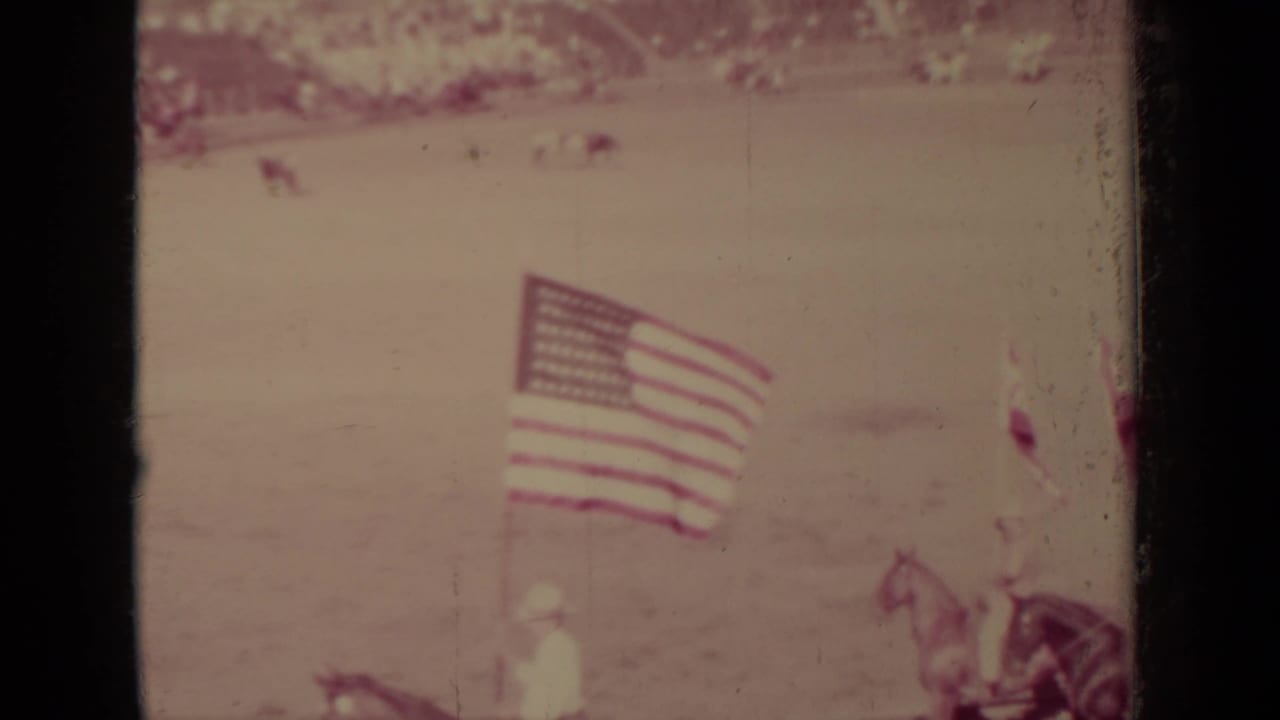 Large American flag and horseback figures appear in the Klamath arena, with the scene softened by faded 8mm color.