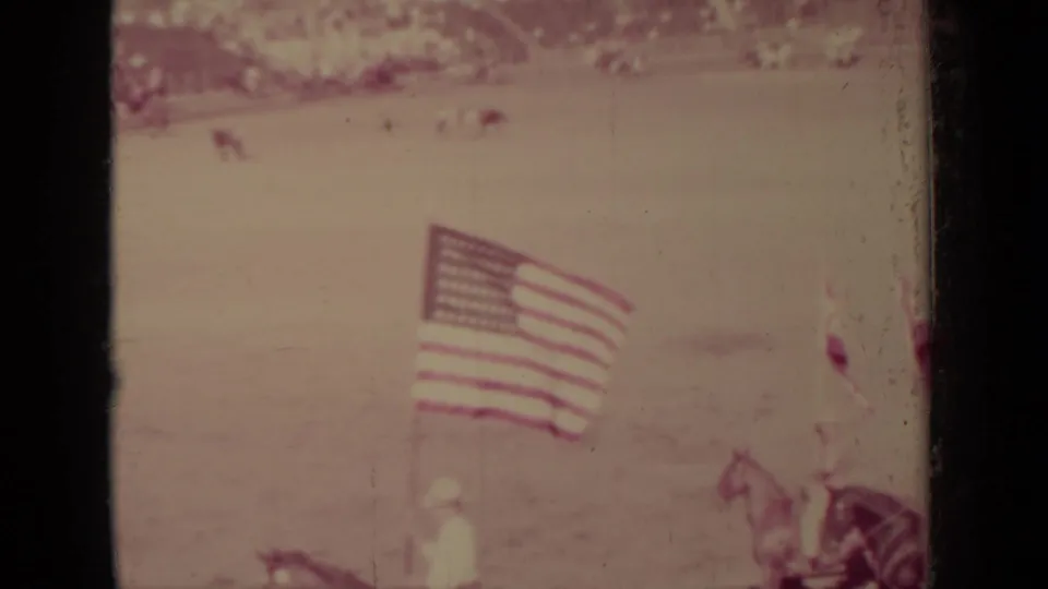 Large American flag and horseback figures appear in the Klamath arena, with the scene softened by faded 8mm color.