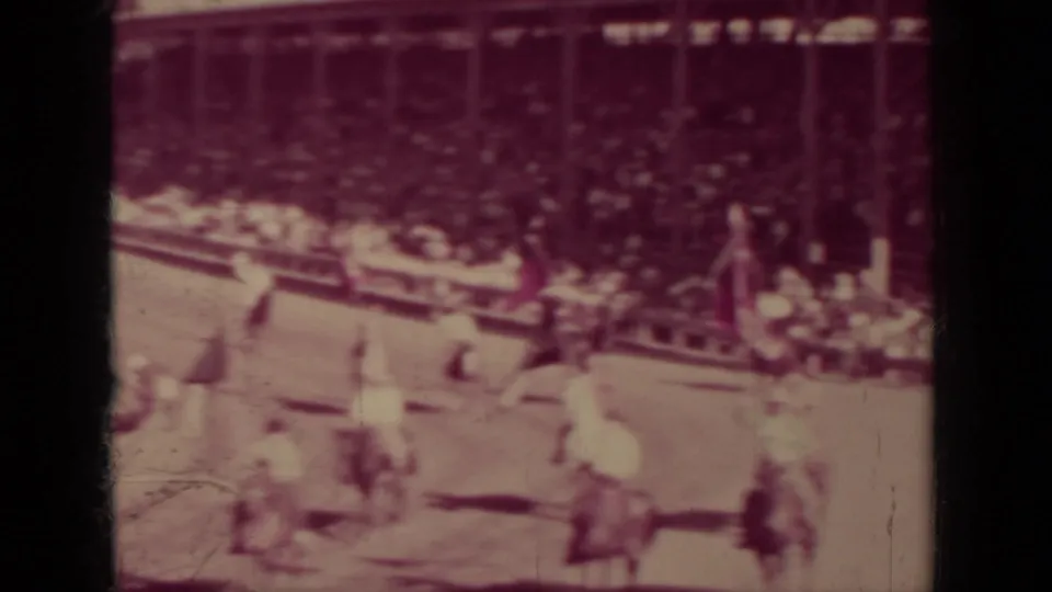 Covered wooden grandstand filled with spectators overlooks riders, flags, and arena rails in 1937 Klamath, California footage.