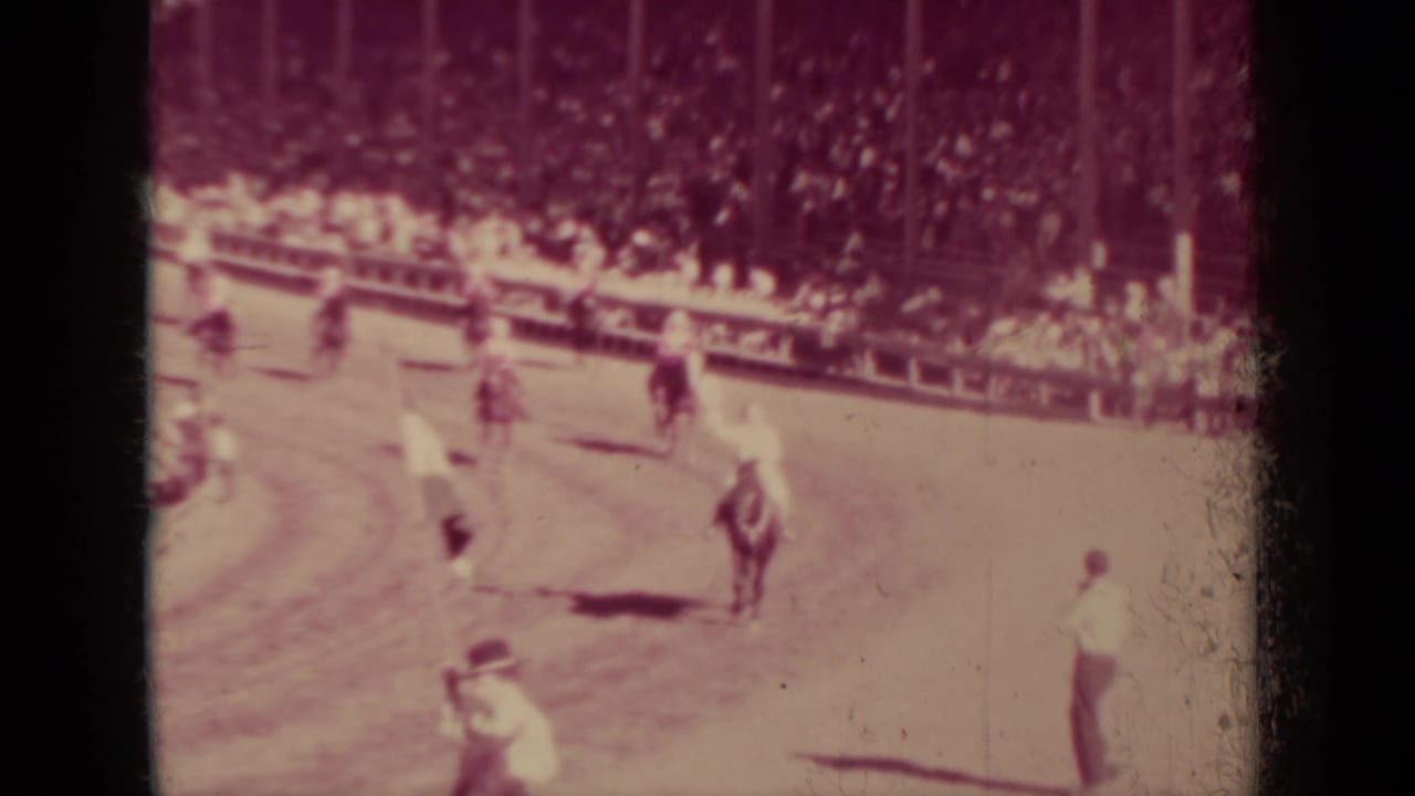 Several riders move across an arena with spectators beyond them.