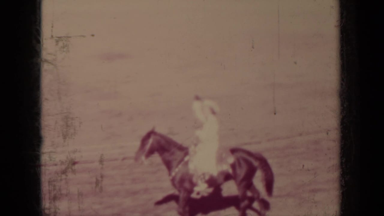Mounted rider in a light shirt and hat passing through a dusty arena.