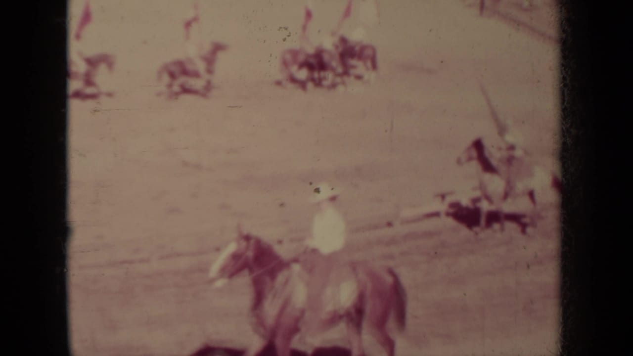 A horseback rider moves across the foreground while distant riders and spectators appear around the arena in Klamath, California.