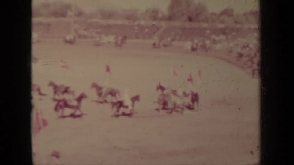 A group of mounted men carrying small flags rides in formation before distant spectators in Klamath, California.