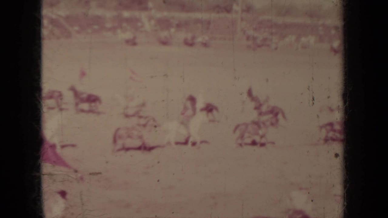 Distant 1937 Klamath arena scene with horseback performers, spectators, and a possible flag or fabric prop in the center area.